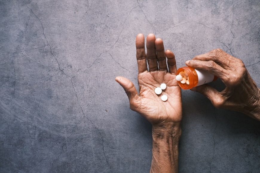 An older persons hands pouring out pills from an orange pill bottle 