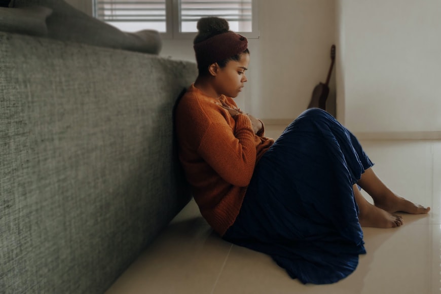 Woman sitting in front of sofa holding her hand to her heart 