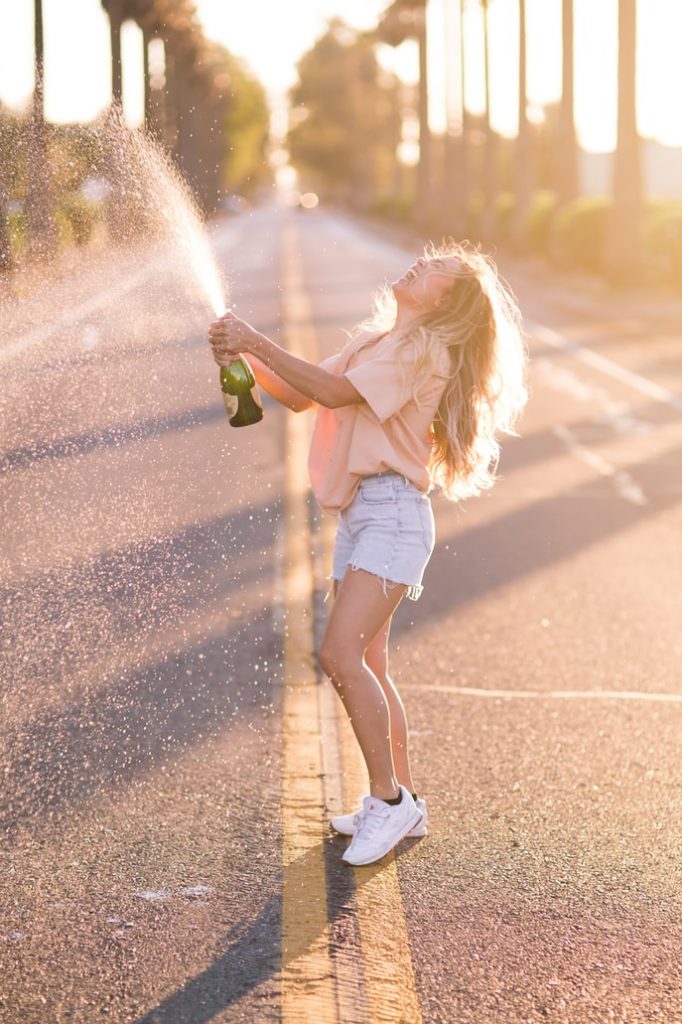 Woman holding a green bottle with liquid spraying out while standing in the middle of a street 