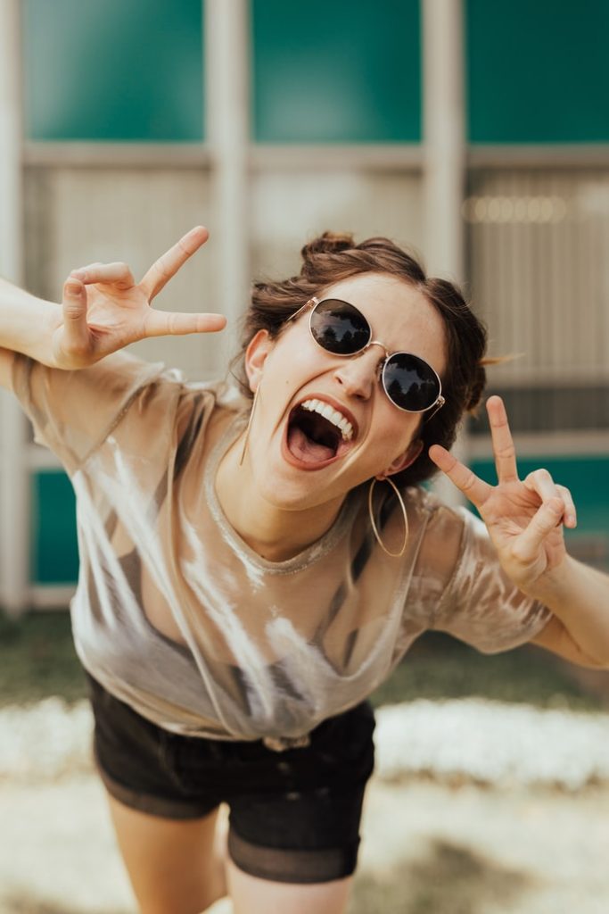 Woman wearing sunglasses and smiling while holding up two peace signs 