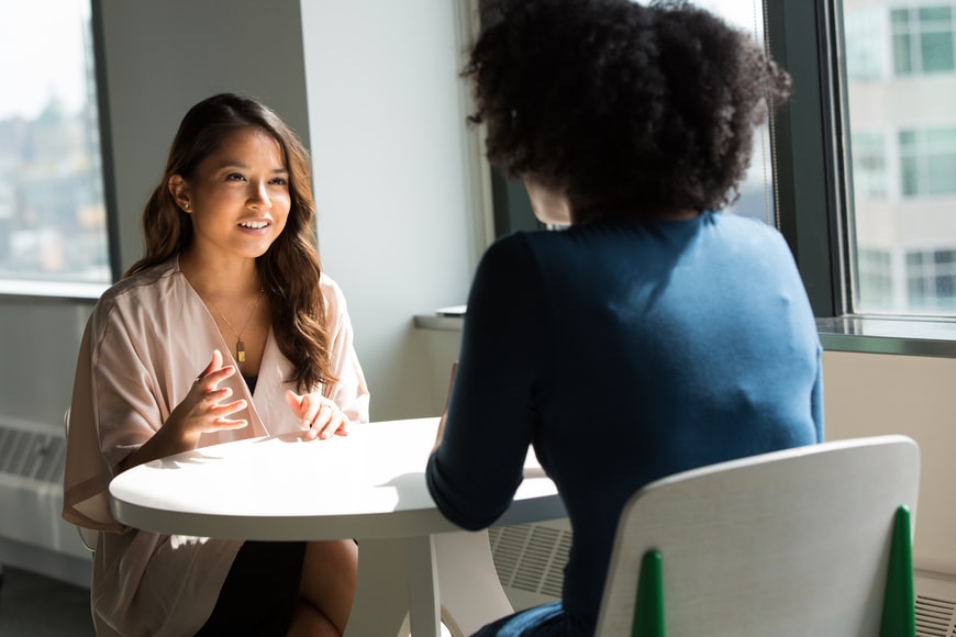 Two women in an office setting talking at a table 