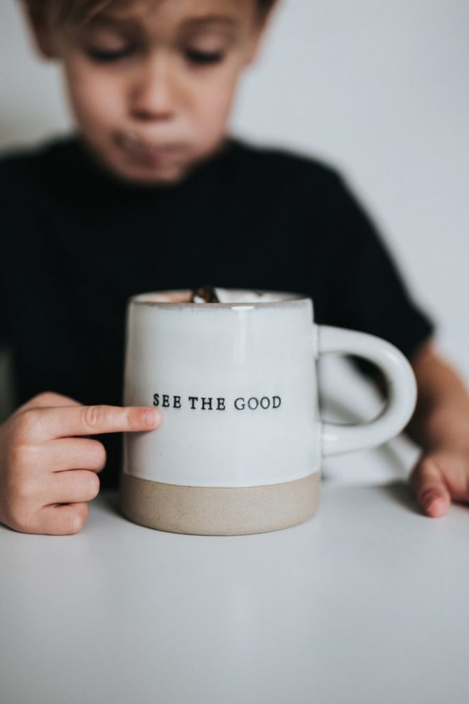 Little boy pointing to a coffee mug with the inscription see the good 