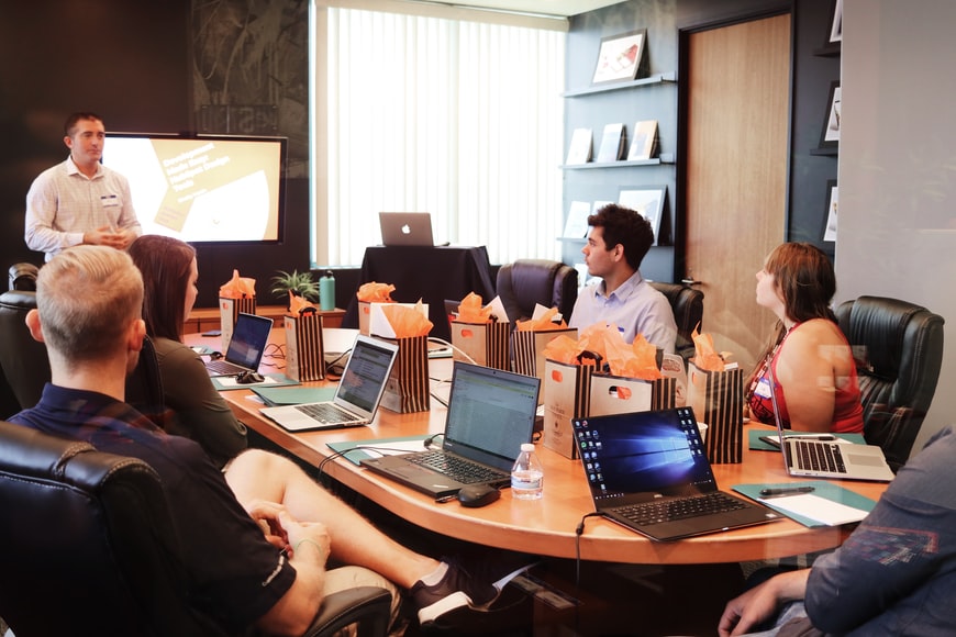 Workplace environment, people sitting around a large table with laptops 