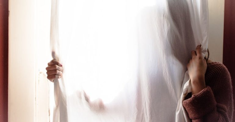 Living with chronic illness, person standing behind a sheer white curtain