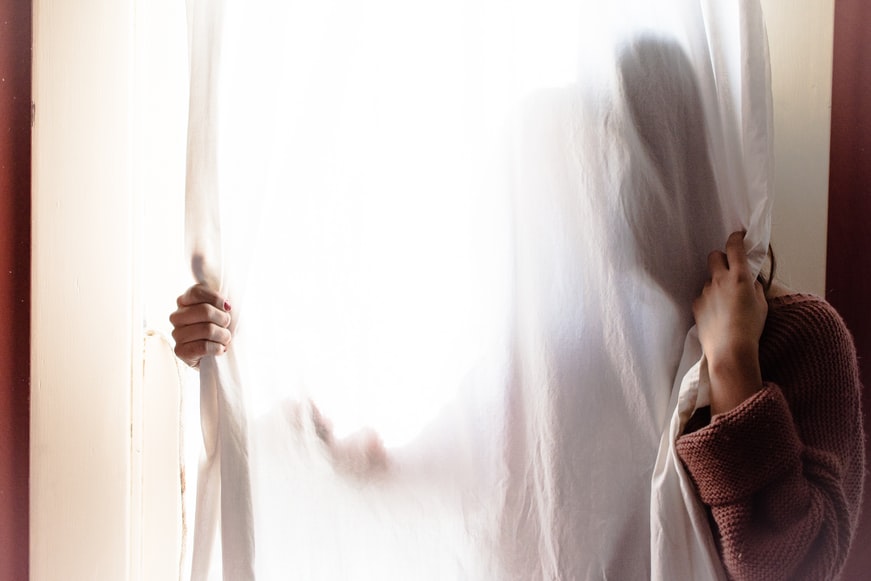 Living with chronic illness, person standing behind a sheer white curtain 