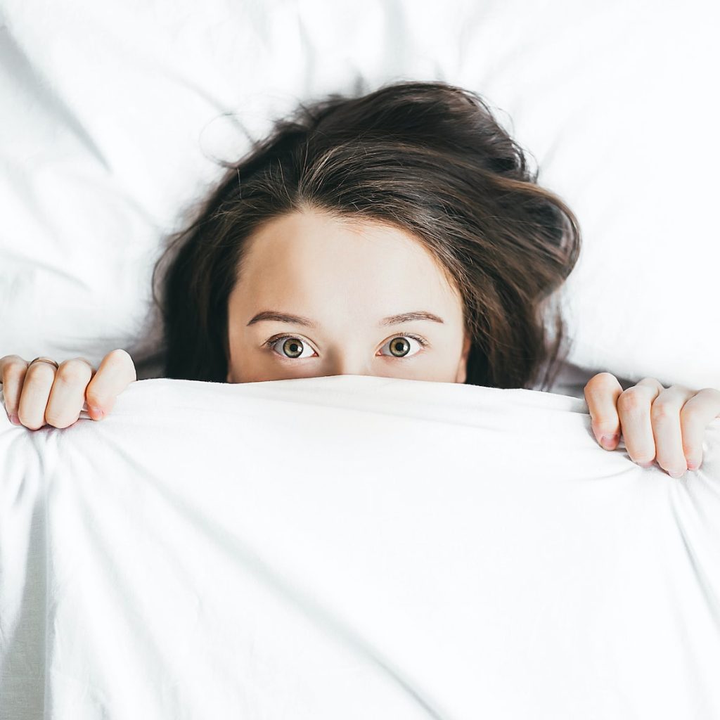 Woman laying in bed covering face with blanket 