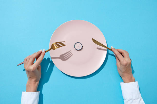 Round watch of six o'clock and woman's hand with fork and knite in agirl's hands on a blue background with shadows. Time to lose weight, eating control or diet concept. 