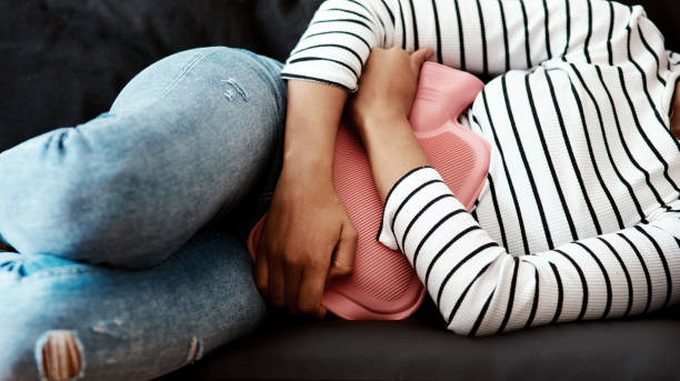 Facts about Endometriosis Cropped shot of a woman holding a hot water bottle against her stomach on the sofa at home