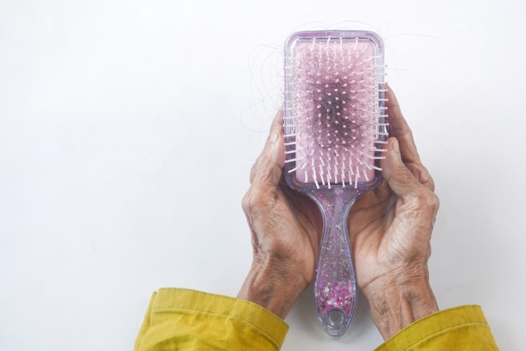 Old hands holding a hair brush full of hair 